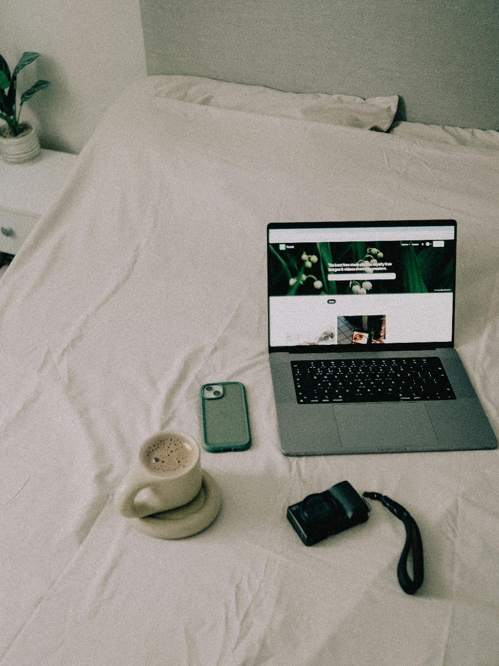 Bed mattress with open laptop, phone, digital camera, and cup of coffee on top