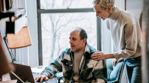 Man sitting on chair with wife leaning above him with her hand on his shoulder